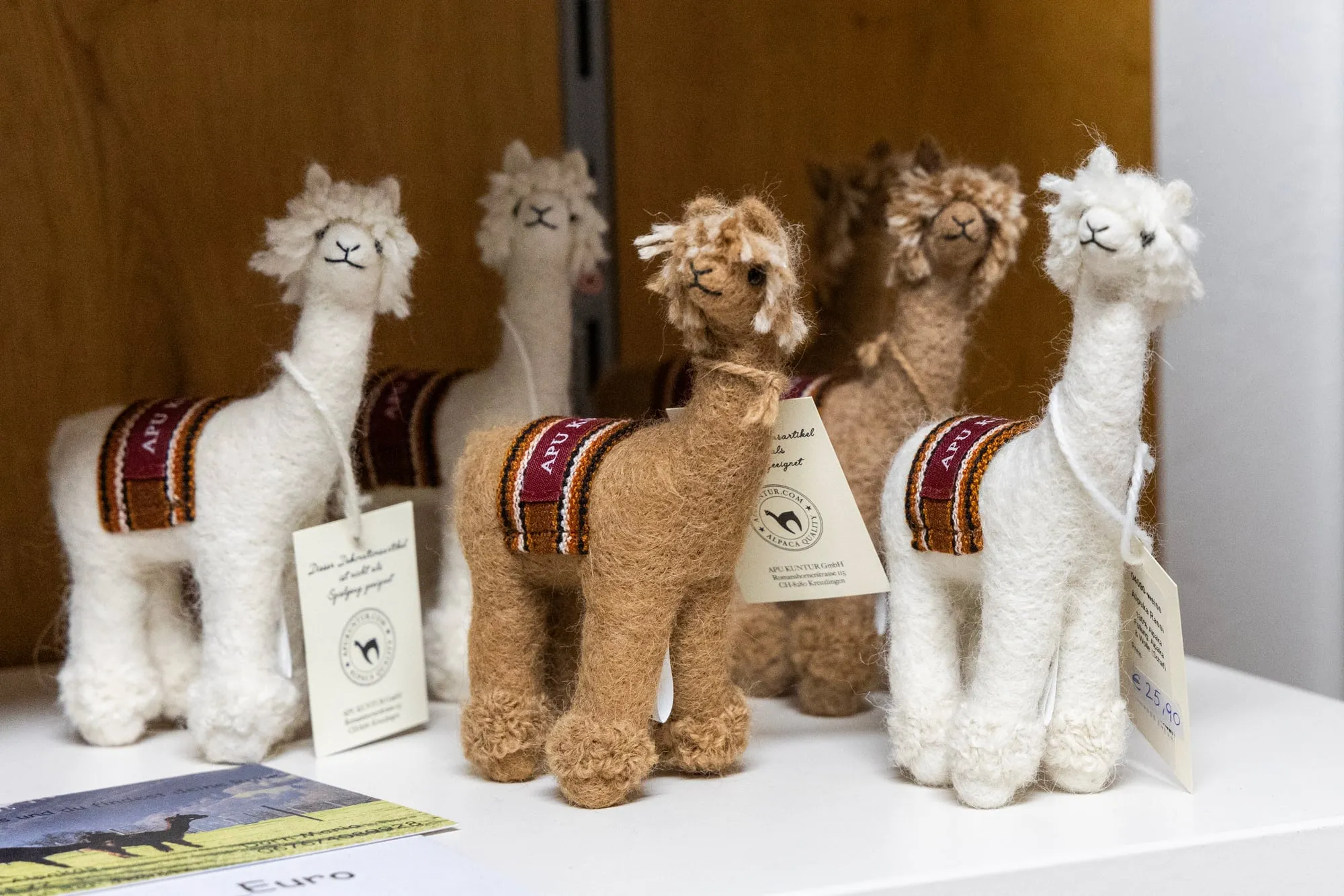 Kleine gefilzte Alpaka-Figuren mit bunten Satteldecken, in einer Reihe aufgestellt.